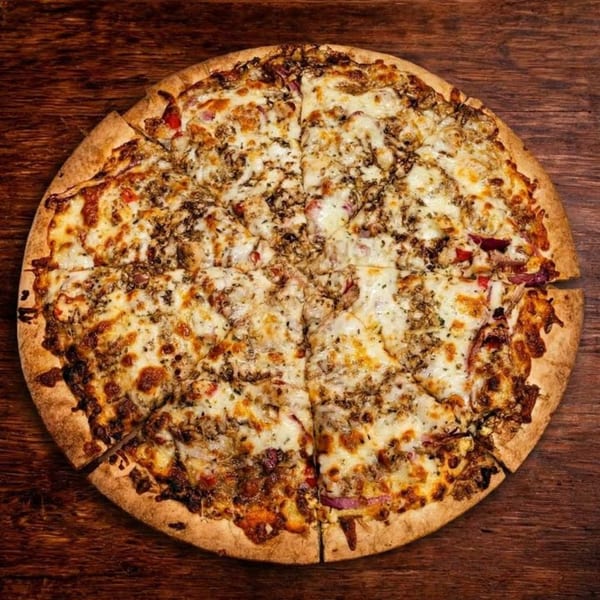 A whole B Antonio's pizza, cut into slices, with melted cheese and various toppings on a wooden table.
