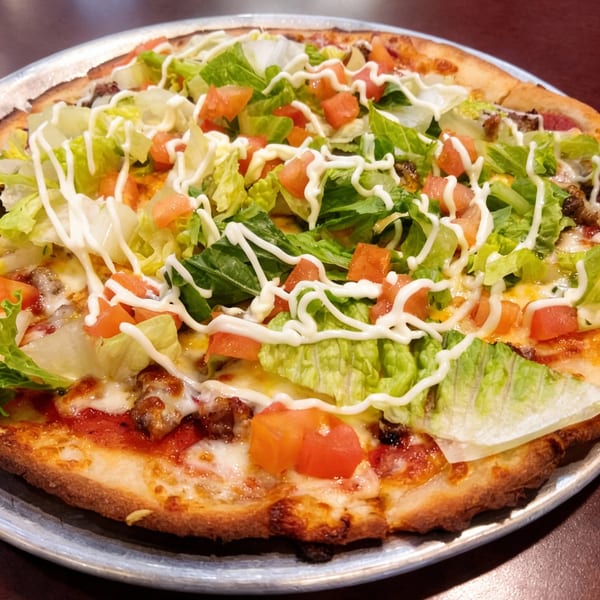 B Antonio's Pizza taco pizza with ground beef, lettuce, diced tomatoes, and a drizzle of white sauce.