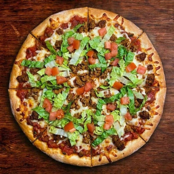 A B Antonio's Pizza with ground meat, melted cheese, lettuce, and diced tomatoes on a wooden table.