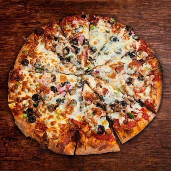 A whole B Antonio's Pizza, sliced, with various toppings including olives, ham, and green peppers.